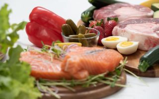A vibrant assortment of fresh salmon, eggs, vegetables, and fruits arranged on a wooden platter.